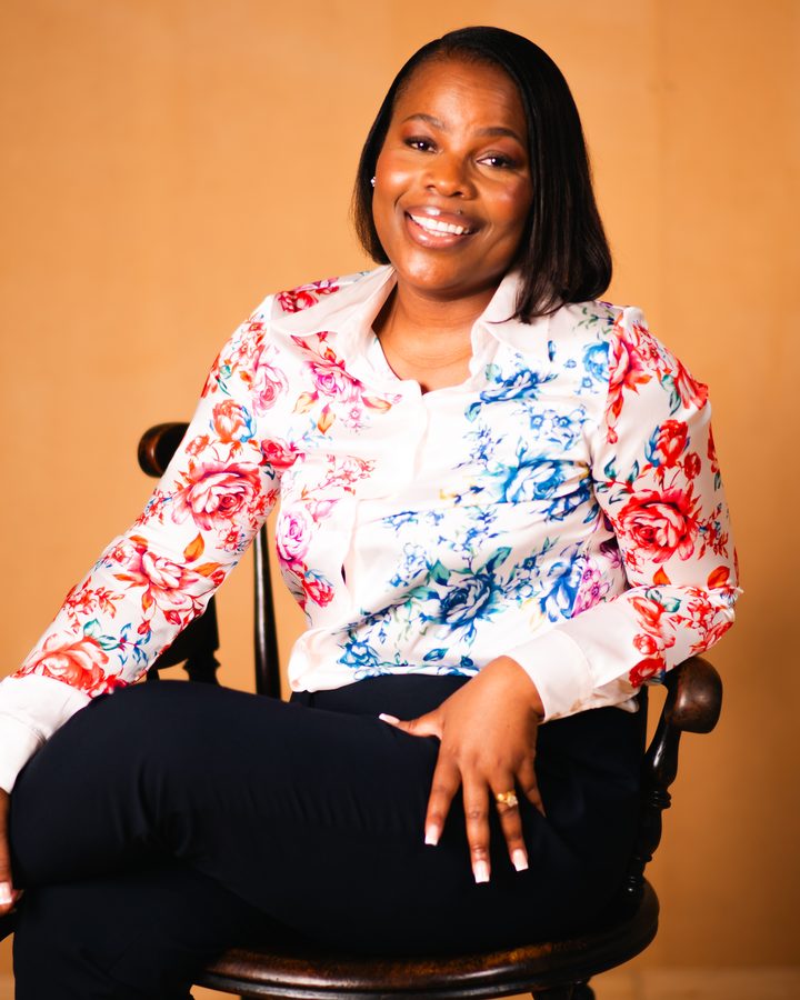 Priscilla Makopa, Director of Healthcare 1st Choice, smiling, seated in a wooden chair