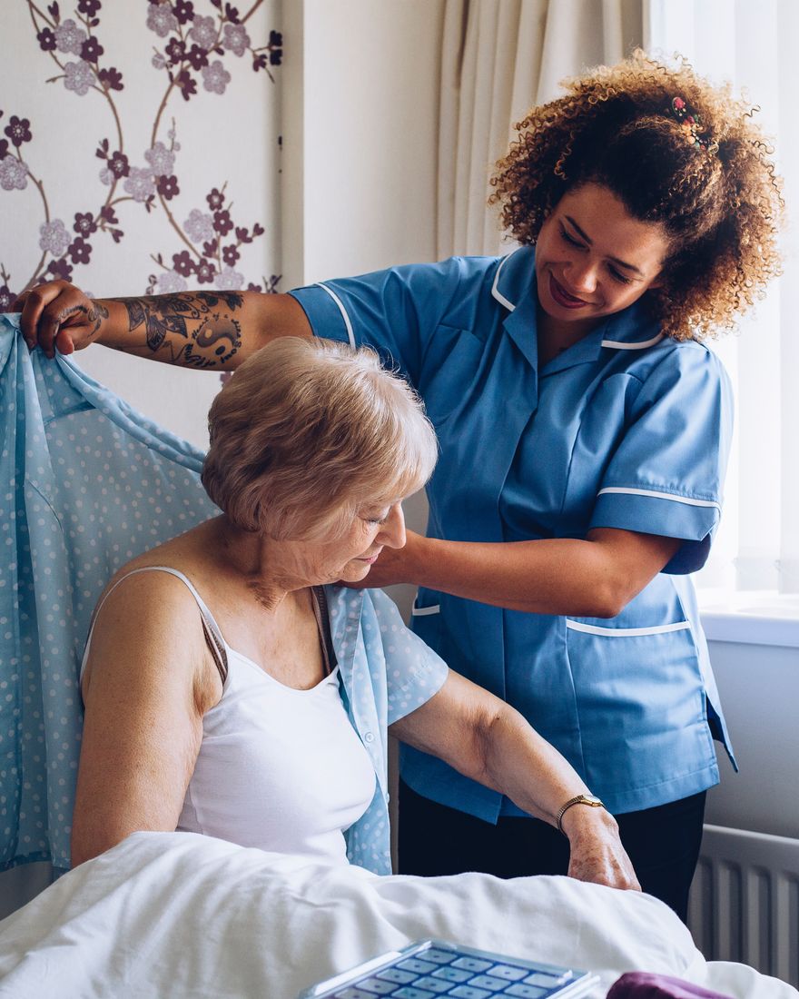 A carer gently helping an older lady get dressed in her bedroom