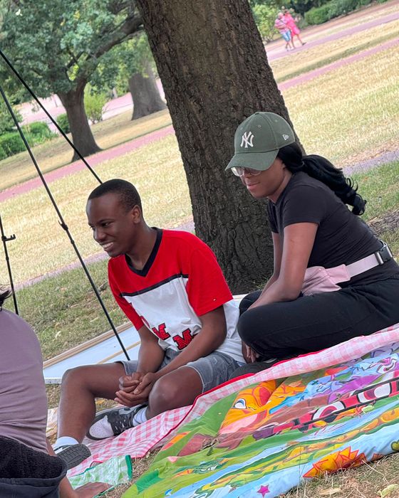 Two people smiling and chatting on a picnic blanket under a tree at our sports day